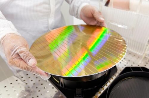 Gloved technician holding a patterned silicon wafer in a cleanroom