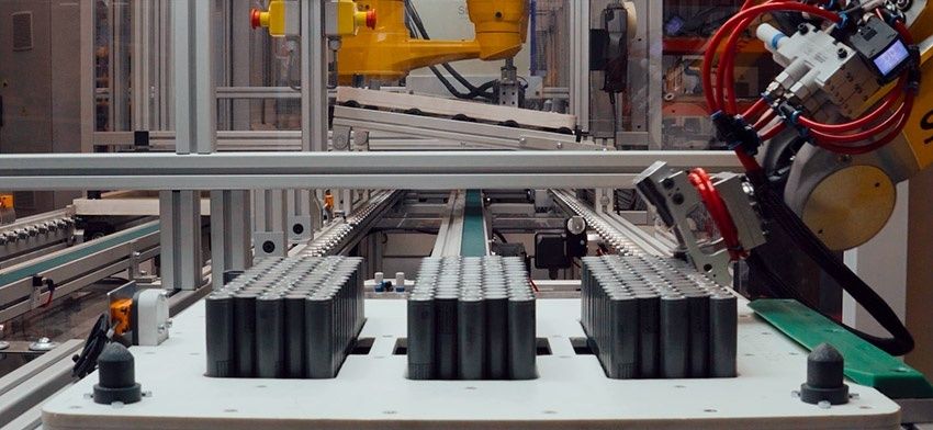 Automated production line with robotic arms handling rows of cylindrical cells