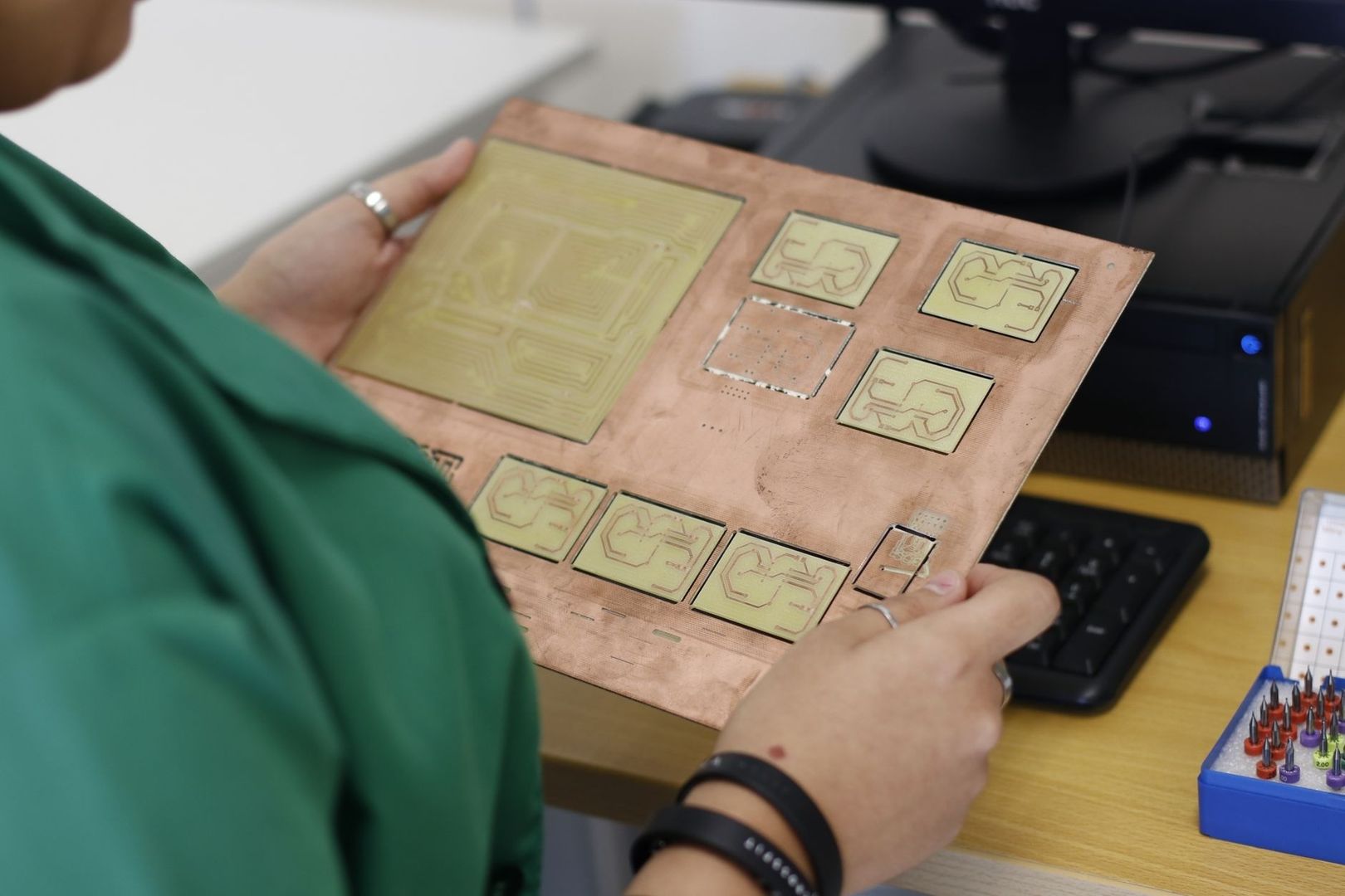 Person holding a panel of patterned circuit prototypes at a workbench